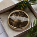 A round ornament with a picture of a distillery or brewery on it, hanging from a string.