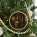 A Christmas tree decorated with ornaments, including a circular ornament featuring a distillery or still, and a string of wooden beads.