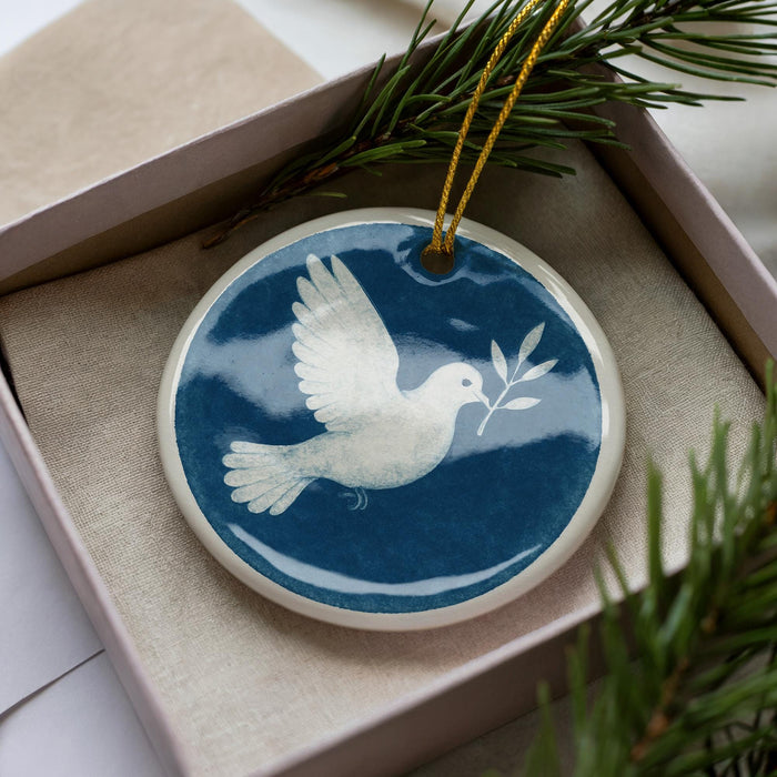 A blue and white ceramic ornament in a box, featuring a white bird in flight with a branch in its beak.