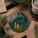 A decorative ornament featuring a green dragon with a castle in the background, set against a night sky with stars and a crescent moon.