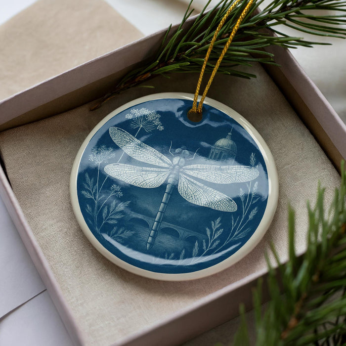 A decorative ornament in a box, featuring a detailed illustration of a dragonfly surrounded by flowers and foliage.
