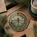 a decorative ceramic ornament with a dragonfly design, placed on a wooden surface alongside a cup of coffee and some pine branches.