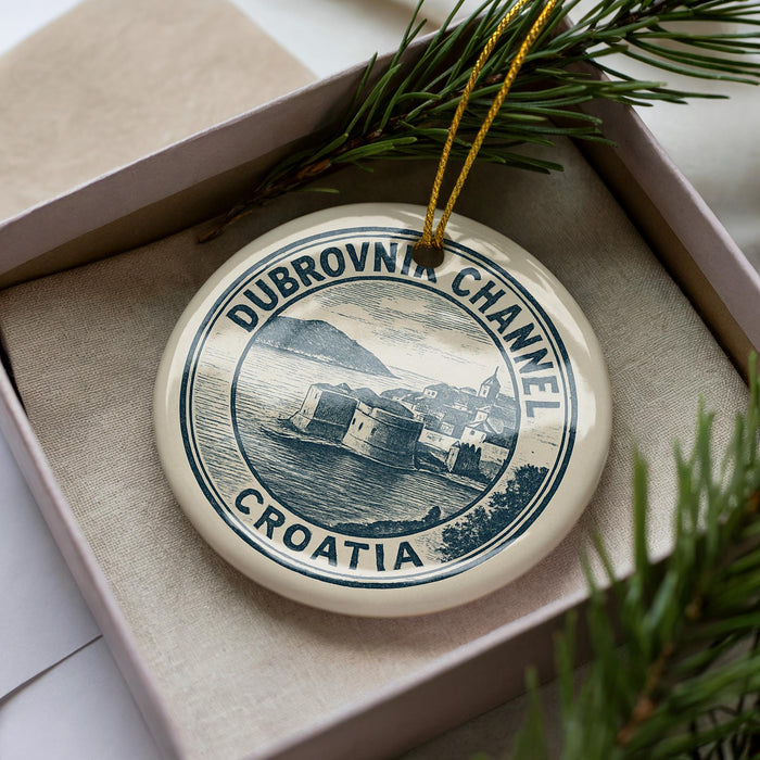 A decorative ornament in a box, featuring a circular design with text and an illustration of a coastal town.