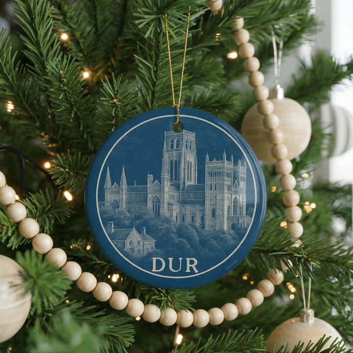 A blue ornament with a drawing of a castle is hanging on a Christmas tree, surrounded by ornaments and lights.