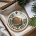 A decorative ornament featuring the image of Edinburgh Castle, a famous landmark in Scotland, is displayed in a box with pine branches.