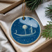 A blue circular ornament with a boat and a moon on a starry night scene, hanging from a string.