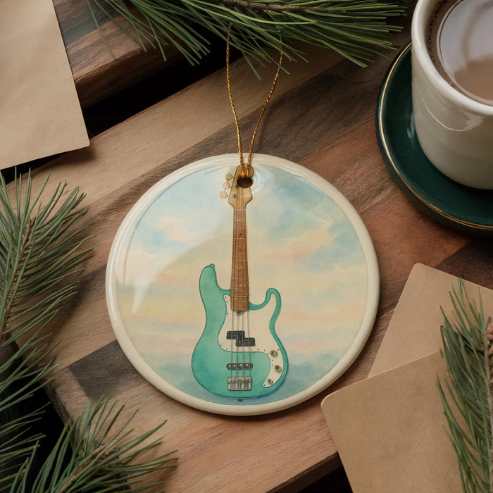 A ceramic ornament featuring a blue bass guitar is displayed on a wooden surface, surrounded by pine branches and a cup of coffee.