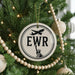 A Christmas tree decorated with ornaments, including a circular ornament with the letters "EWR" and a silhouette of the Statue of Liberty.