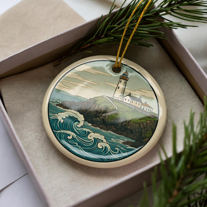 A decorative ornament featuring a lighthouse on a cliff overlooking the ocean, surrounded by pine branches.