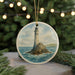 A round ornament featuring a lighthouse on a rocky island, surrounded by water, is displayed in front of a Christmas tree with lights.