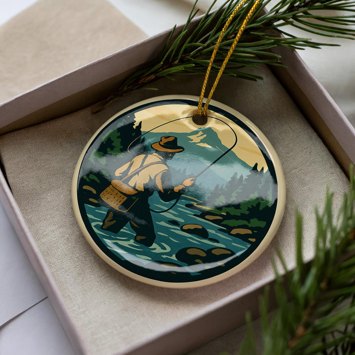 A round ornament depicting a person fishing in a river, surrounded by pine branches and greenery.