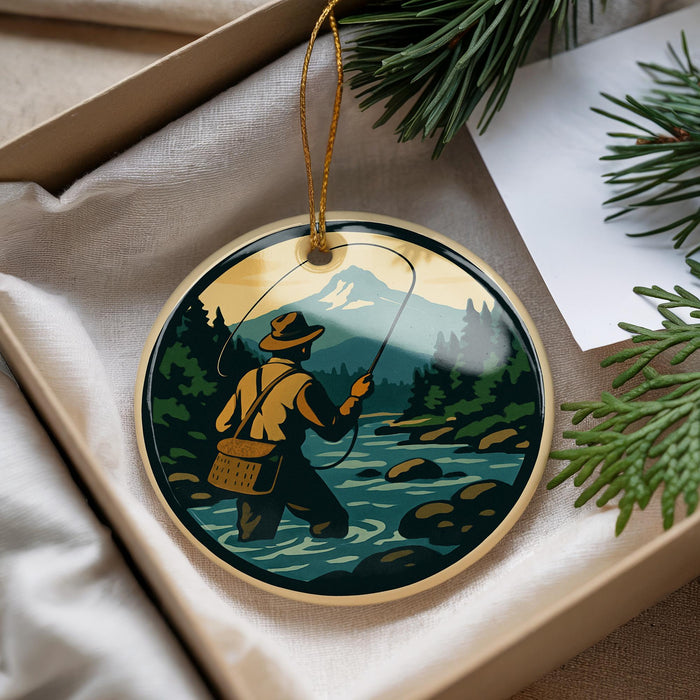 A round ornament depicting a person fishing in a river, surrounded by pine trees and mountains.