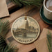 A decorative ornament featuring a cityscape with a bridge, hanging on a wooden surface.