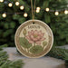 A round ornament with a floral design featuring a pink lotus flower and green leaves, hanging from a string.