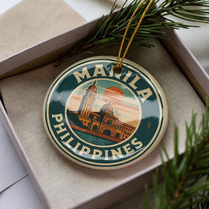 A circular ornament with the text "MANILA PHILIPPINES" and an illustration of a building, placed in a box with pine branches.