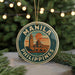 A round ornament with the text "MANILA PHILIPPINES" and an illustration of a building, likely representing the Manila skyline, is displayed in front of a Christmas tree with twinkling lights.
