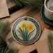 a decorative ceramic ornament with a floral design, placed on a wooden surface alongside a cup of coffee and some pine branches.