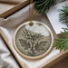 A decorative ornament featuring a chrysanthemum flower is displayed in a box, surrounded by pine branches and a white card.