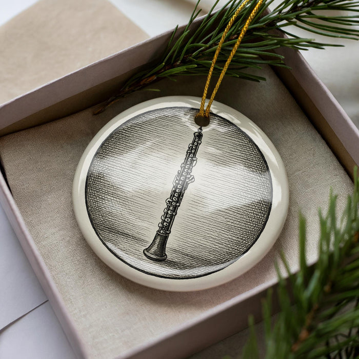A ceramic ornament in the shape of a flute, displayed in a box with pine branches.