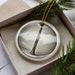 A ceramic ornament in the shape of a flute, displayed in a box with pine branches.