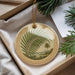 A decorative ornament with a palm tree design is displayed in a box, surrounded by pine branches and a white card.