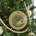 A round ornament with a palm tree design hangs from a Christmas tree, surrounded by other ornaments and lights.