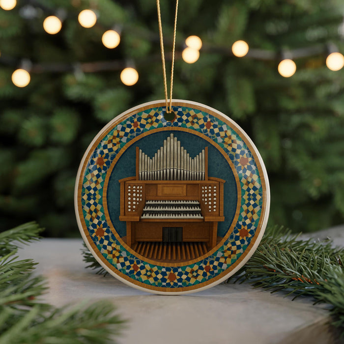 A circular ornament featuring an organ with pipes and a decorative border, hanging on a string and surrounded by pine branches with lights in the background.