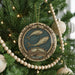 A decorative ornament with a fish design hangs on a Christmas tree, surrounded by lights and ornaments.