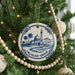 A Christmas tree decorated with ornaments, including a circular ornament with a blue and white design depicting a mosque and palm trees, surrounded by white beads.