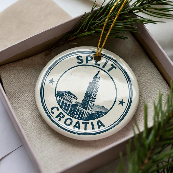 A circular ornament with the text "SPLIT" and "CRAATIA" printed on it, surrounded by a decorative border. The ornament is placed inside a box with pine branches.