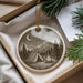 A decorative ornament featuring a camping scene with a tent, campfire, and mountains in the background, hanging from a string.