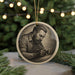 A circular ornament featuring a detailed engraved image of a man with a beard, sitting at a table and holding a book.