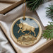A decorative ornament featuring a bull and the word "Taurus" on a circular background, placed in a box with pine branches.