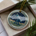 A decorative ornament in a box, featuring a telescope and a starry night sky background.