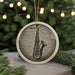 A ceramic ornament featuring a saxophone is displayed on a table, with a blurred background of a Christmas tree and twinkling lights.