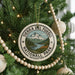 A round ornament on a Christmas tree, featuring the text "TERRA DEL FUEGO NATIONAL PARK ARGENTINA" and a mountain landscape.