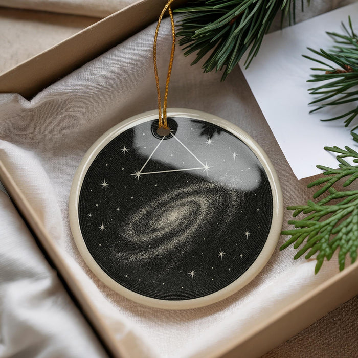 A decorative ornament in a box, featuring a starry night sky design with a spiral galaxy.