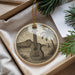 A decorative ornament featuring a guitar and a tropical landscape, placed in a box with pine branches.