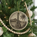 A Christmas tree decorated with a circular ornament featuring a guitar and a palm tree, surrounded by beaded ornaments and twinkling lights.