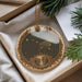 A decorative ornament with a starry night sky and a bear is displayed in a box, surrounded by pine branches.