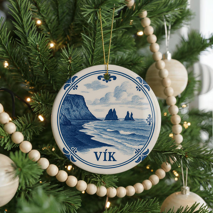 A Christmas tree decorated with a blue and white ornament featuring a coastal scene, surrounded by ornaments and lights.