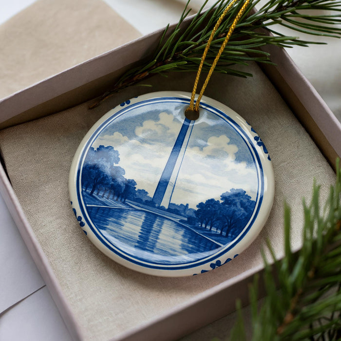 A decorative ornament in the shape of a blue and white plate with a landscape scene, featuring a tall tower in the background.