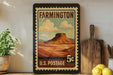 A framed vintage postage stamp depicting a mountain landscape hangs on a wall, surrounded by kitchen utensils and a potted plant.