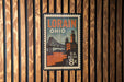 A vintage-style postage stamp from the United States, featuring an illustration of a bridge and buildings, mounted on a wooden wall.