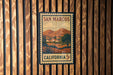 A framed poster of San Marcos, California, with a vintage-style illustration of a rural landscape and mountains.