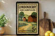 A vintage postage stamp from the United States, featuring a rural scene with a house, road, and trees, is displayed on a wall next to a wooden cutting board and some lemons.