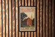 A vintage U.S. postage stamp featuring a red brick house with a steeple, mounted on a wooden wall.