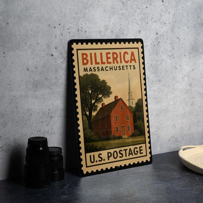 A vintage-style stamp depicting a red brick house with a church steeple, placed on a countertop next to some black camera lenses.