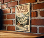 A vintage-style postage stamp from Colorado, featuring a mountain landscape and a cabin, is displayed on a brick wall.
