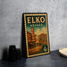 A vintage-style metal sign for Elko, Nevada, featuring a colorful illustration of the Elko Hotel and surrounding buildings.